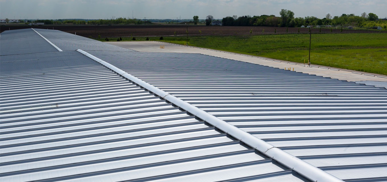 Standing seam metal roof with a raised ridge cap detail, overlooking a parking lot and green fields in the distance.